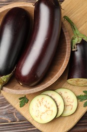 Photo of Whole and cut eggplants with parsley on wooden table, flat lay