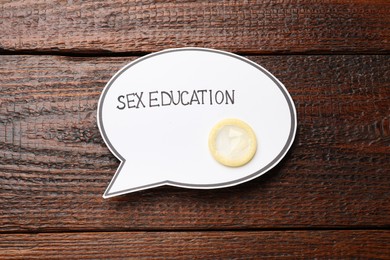 Photo of Speech bubble with phrase Sex Education and condom on wooden background, top view