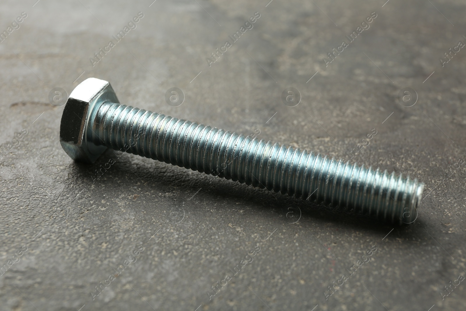 One metal bolt on grey table, closeup Photo of One metal bolt on grey table, closeup