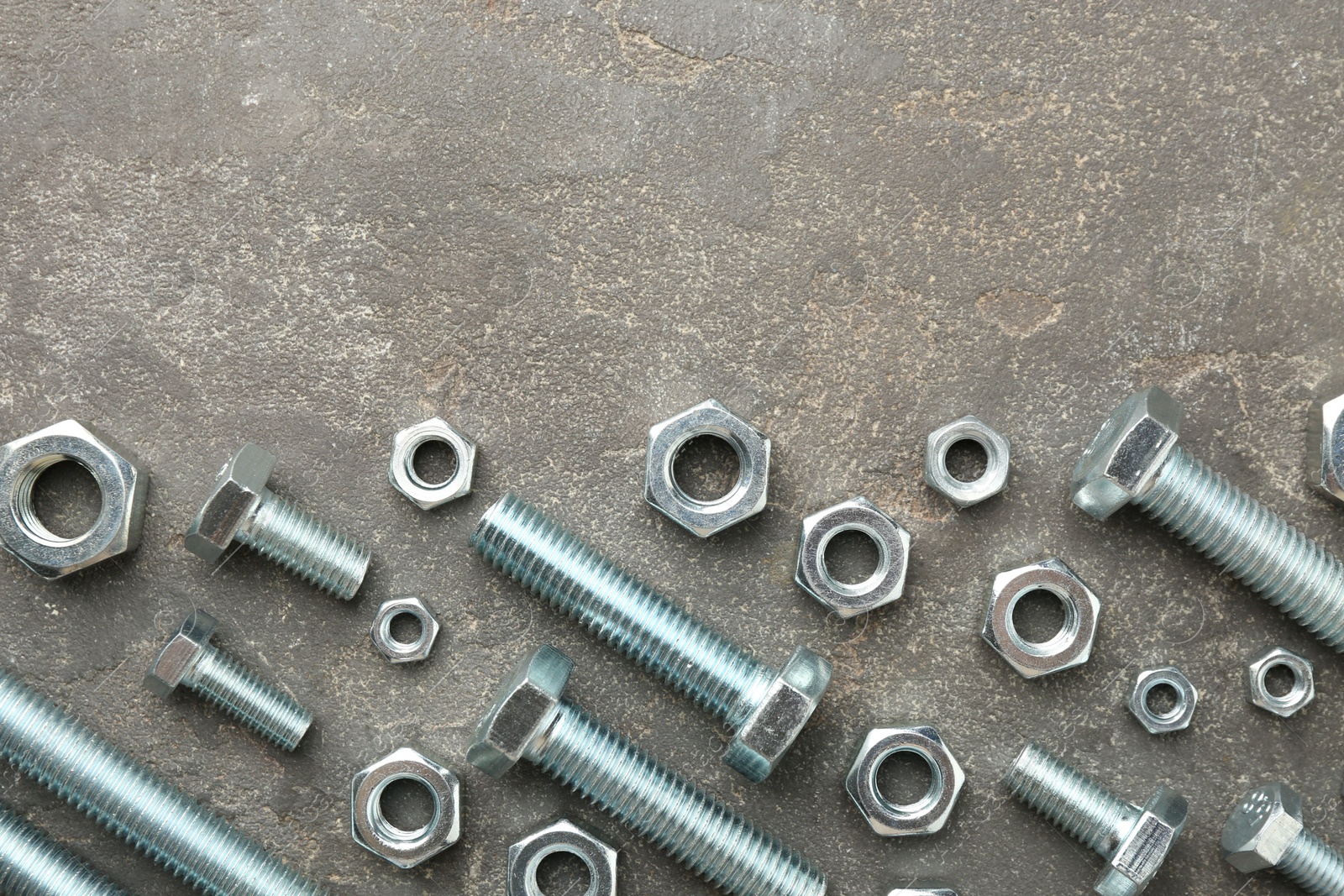 Metal bolts and nuts on grey table, flat lay. Space for text Photo of Metal bolts and nuts on grey table, flat lay. Space for text