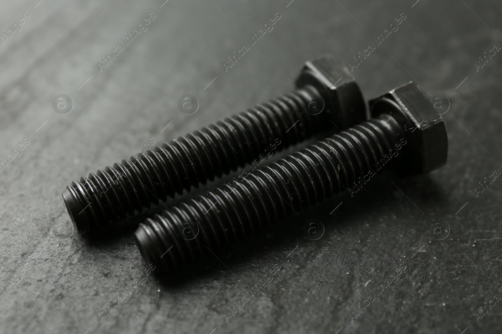 Two metal bolts on black table, closeup Photo of Two metal bolts on black table, closeup