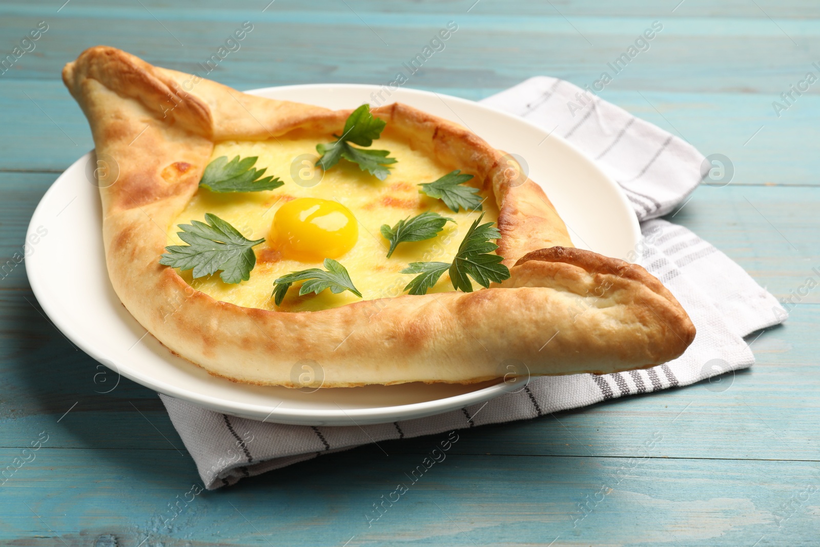 Tasty khachapuri with cheese, egg and parsley on light blue wooden table, closeup Photo of Tasty khachapuri with cheese, egg and parsley on light blue wooden table, closeup