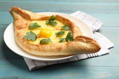 Photo of Tasty khachapuri with cheese, egg and parsley on light blue wooden table, closeup