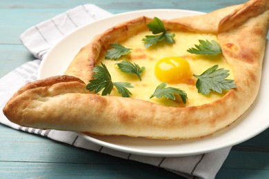 Photo of Tasty khachapuri with cheese, egg and parsley on light blue wooden table, closeup