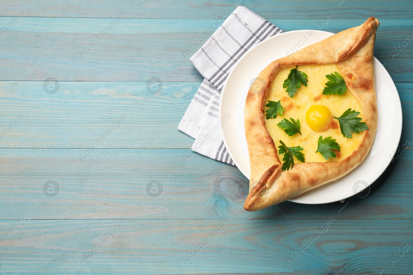 Tasty khachapuri with cheese, egg and parsley on light blue wooden table, top view. Space for text Photo of Tasty khachapuri with cheese, egg and parsley on light blue wooden table, top view. Space for text