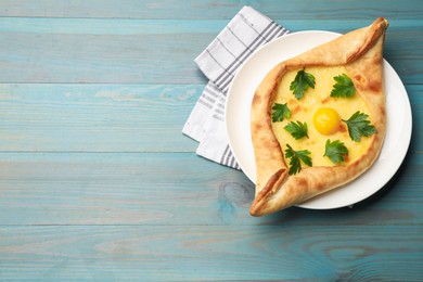 Photo of Tasty khachapuri with cheese, egg and parsley on light blue wooden table, top view. Space for text