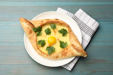 Photo of Tasty khachapuri with cheese, egg and parsley on light blue wooden table, top view