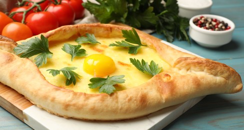 Photo of Tasty khachapuri with cheese, egg, parsley, tomatoes and spices on light blue wooden table, closeup
