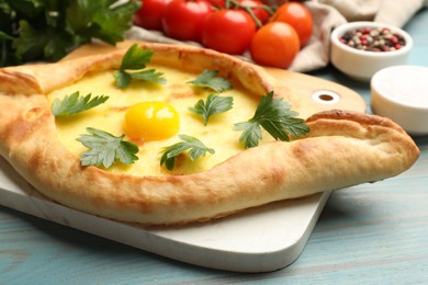 Photo of Tasty khachapuri with cheese, egg, parsley, tomatoes and spices on light blue wooden table, closeup