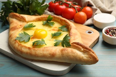 Photo of Tasty khachapuri with cheese, egg, parsley, tomatoes and spices on light blue wooden table, closeup