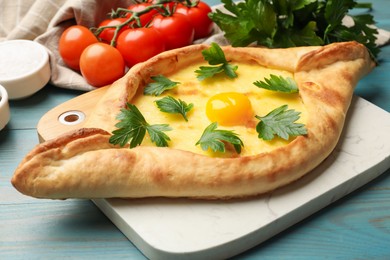 Photo of Tasty khachapuri with cheese, egg, parsley, tomatoes and spices on light blue wooden table, closeup