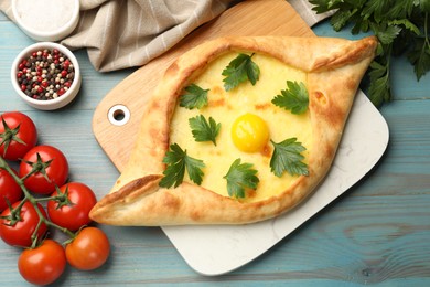 Photo of Tasty khachapuri with cheese, egg, parsley, tomatoes and spices on light blue wooden table, flat lay