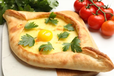 Photo of Tasty khachapuri with cheese, egg, parsley and tomatoes on white table, closeup