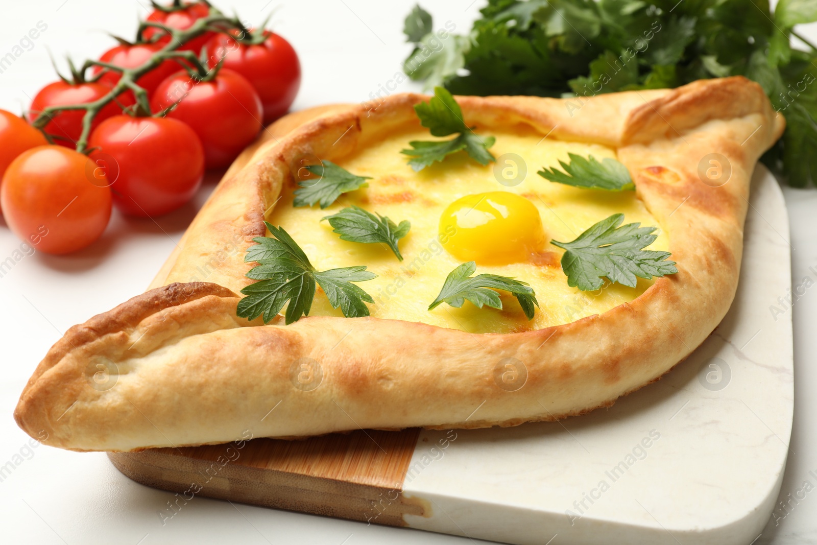 Tasty khachapuri with cheese, egg, parsley and tomatoes on white table, closeup Photo of Tasty khachapuri with cheese, egg, parsley and tomatoes on white table, closeup