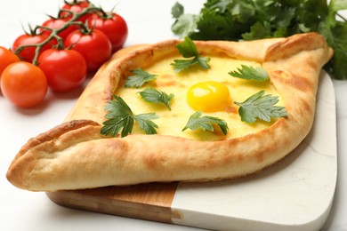 Photo of Tasty khachapuri with cheese, egg, parsley and tomatoes on white table, closeup