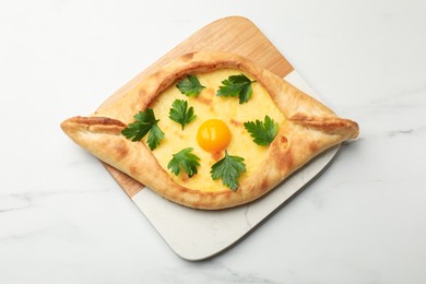 Photo of Tasty khachapuri with cheese, egg and parsley on white marble table, top view