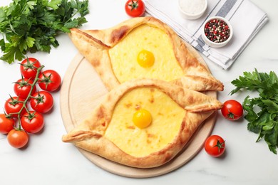 Photo of Tasty khachapuris with cheese, eggs, tomatoes, parsley and spices on white marble table, flat lay