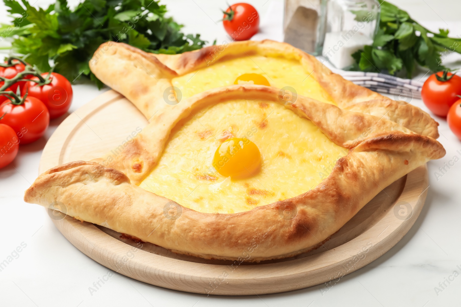 Photo of Tasty khachapuris with cheese, eggs, tomatoes, parsley and spices on white marble table, closeup
