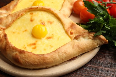 Photo of Tasty khachapuris with cheese, eggs, tomatoes and parsley on wooden table, closeup
