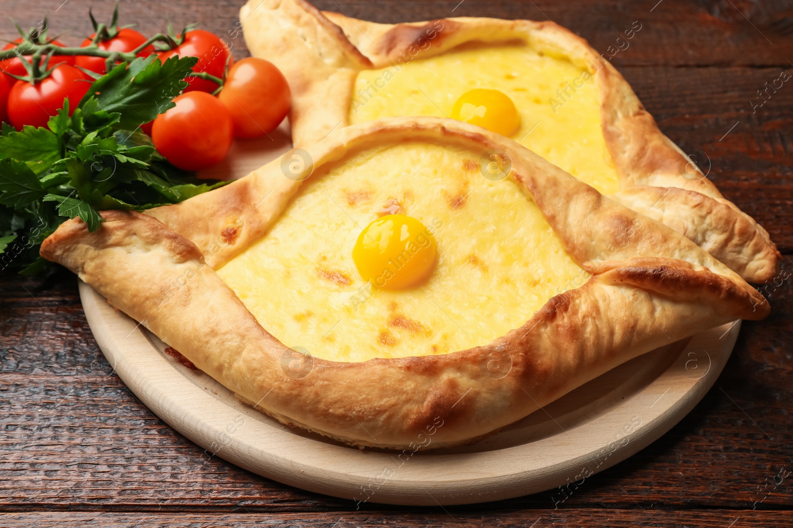 Photo of Tasty khachapuris with cheese, eggs, tomatoes and parsley on wooden table, closeup