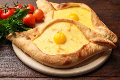 Photo of Tasty khachapuris with cheese, eggs, tomatoes and parsley on wooden table, closeup