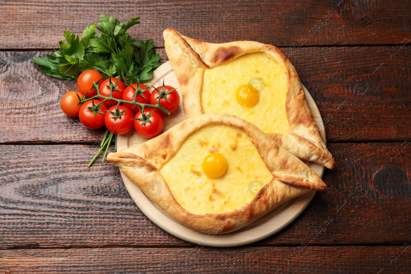 Photo of Tasty khachapuris with cheese, eggs, tomatoes and parsley on wooden table, flat lay