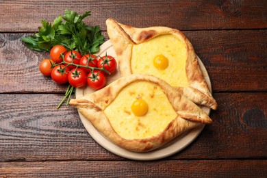 Photo of Tasty khachapuris with cheese, eggs, tomatoes and parsley on wooden table, flat lay