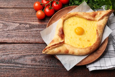 Photo of Tasty khachapuri with cheese, egg, tomatoes and parsley on wooden table, flat lay. Space for text