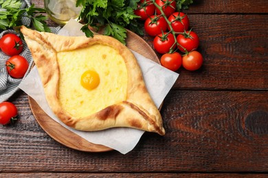 Photo of Tasty khachapuri with cheese, egg, tomatoes and parsley on wooden table, flat lay. Space for text