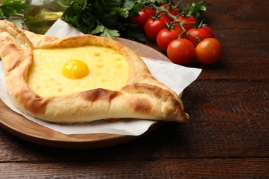 Photo of Tasty khachapuri with cheese, egg, tomatoes and parsley on wooden table, closeup. Space for text