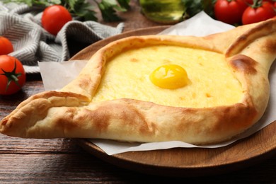 Photo of Tasty khachapuri with cheese, egg, tomatoes and parsley on wooden table, closeup