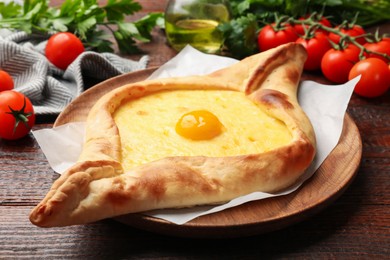 Photo of Tasty khachapuri with cheese, egg, tomatoes and parsley on wooden table, closeup