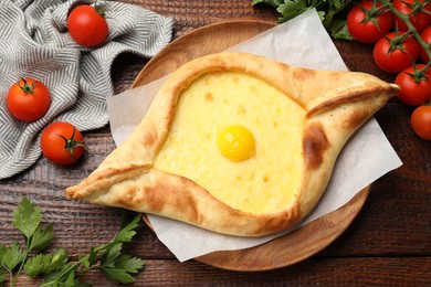 Photo of Tasty khachapuri with cheese, egg, tomatoes and parsley on wooden table, flat lay