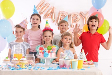 Photo of Birthday celebration. Kids at table with tasty cake and different treats in festive decorated room