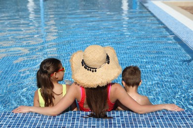 Photo of Woman with her children in swimming pool, back view. Summer vacation