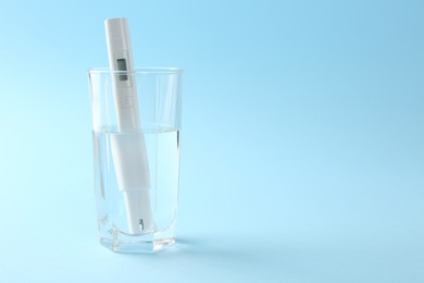 Photo of Nitrate tester in glass of water on light blue background, space for text