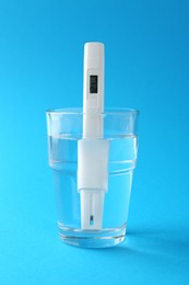 Photo of Nitrate tester in glass of water on light blue background, closeup