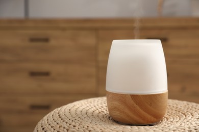 Photo of Modern aroma lamp on wicker surface indoors. Space for text