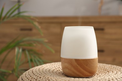 Photo of Modern aroma lamp on wicker surface indoors. Space for text