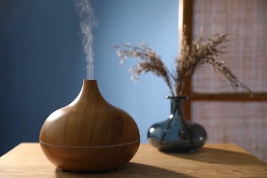 Photo of Modern aroma lamp and dry plants in vase on wooden table indoors, closeup