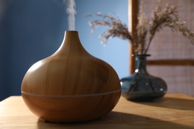 Photo of Modern aroma lamp and dry plants in vase on wooden table indoors, closeup
