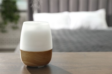 Photo of Modern aroma lamp on wooden table indoors. Space for text