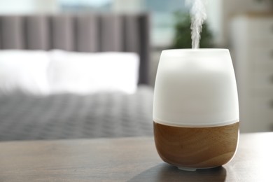 Photo of Modern aroma lamp on wooden table indoors. Space for text