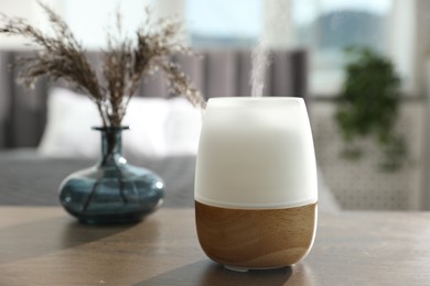 Photo of Modern aroma lamp and dry plants in vase on wooden table indoors