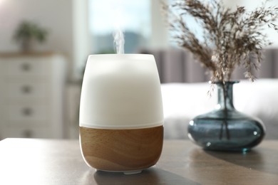 Photo of Modern aroma lamp and dry plants in vase on wooden table indoors