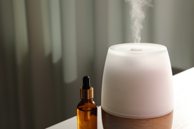 Photo of Modern aroma lamp and bottle of essential oil on table indoors, closeup