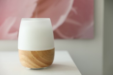 Photo of Modern aroma lamp on white wooden table, closeup. Space for text