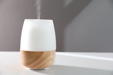 Photo of Modern aroma lamp on white wooden table against gray background. Space for text