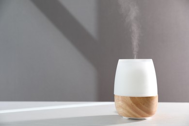 Photo of Modern aroma lamp on white wooden table against gray background. Space for text