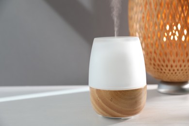 Photo of Modern aroma lamp on white wooden table indoors. Space for text